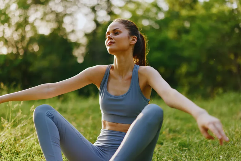 Young woman practicing yoga outdoors in a green park, wearing athletic attire and expressing serenity, embodying health and wellness, perfect for fitness themes