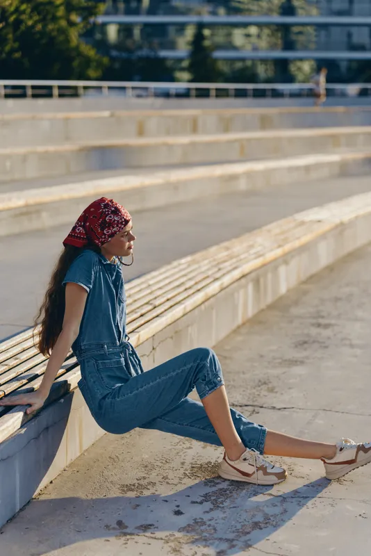 Lifestyle woman in modern boho-western denim street style wearing a red bandana, relaxed outdoors in warm natural light with film color tones and casual footwear.