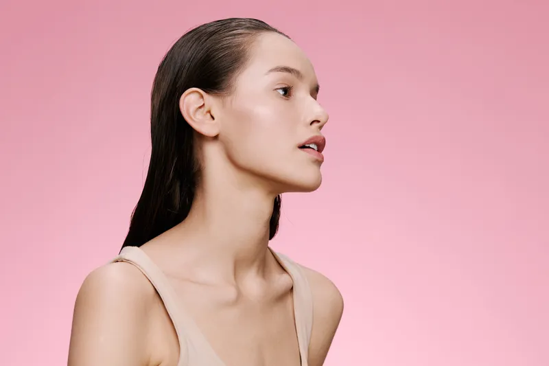 Profile portrait of a young woman with a natural look against a soft pink background, showcasing healthy skin and beauty, ideal for skincare and cosmetics advertising