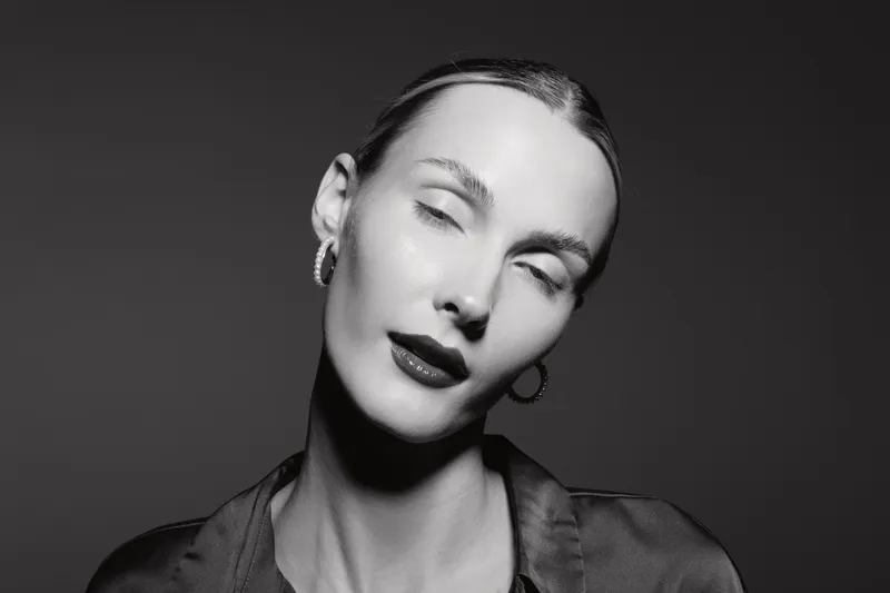Close-up portrait of a fair skinned Caucasian woman with slicked hair and dark lipstick posing with closed eyes in black and white studio lighting. Concept of beauty and fashion.