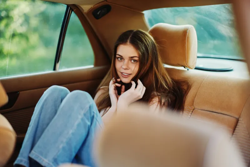 A young woman with long hair sitting comfortably in a car, wearing casual clothing and smiling, capturing a relaxed and happy mood, perfect for lifestyle concept photography.