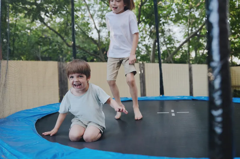 Joyful children jumping on a trampoline surrounded by greenery, showcasing their playful spirit and excitement in a sunny outdoor setting.
