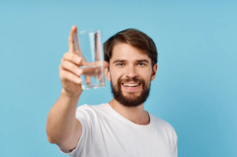 Красивый мужчина со стаканом воды на синем фоне