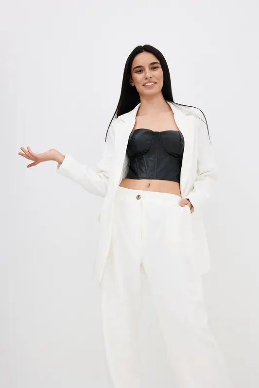 young woman in white suit and black top smiling confidently against plain background, casual fashion style, relaxed pose, modern outfit.