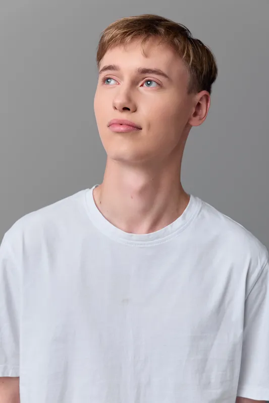 Young man wearing a white t shirt in casual wear, studio lighting highlights every detail against a neutral background, head and shoulders composition, focused expression and fashion pose suitable