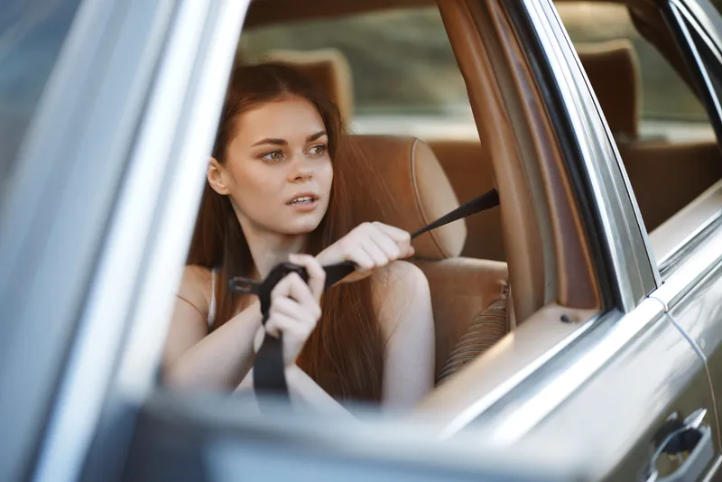 Young woman fastening her seatbelt in a car, reflecting safety and care while enjoying a scenic drive. The warm tones emphasize the journey's significance.
