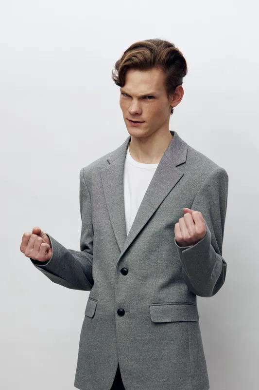 Уверенный молодой бизнесмен в синем костюме позирует стильно на сером фоне