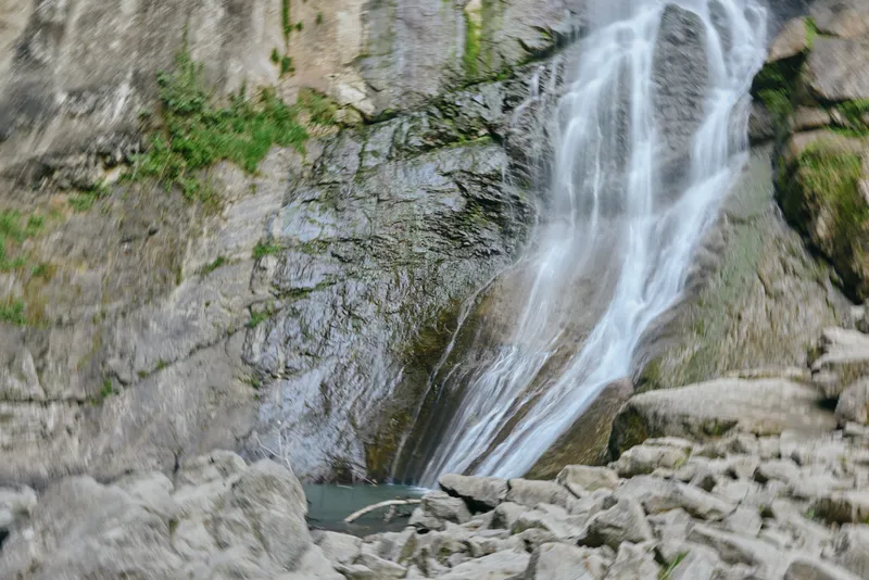 waterfalls in nature, cascading water flowing over rocky cliff surrounded by greenery in a tranquil outdoor environment, fresh and peaceful atmosphere.