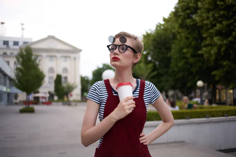 Привлекательная женщина в очках идет на улице, держа в руках кофе
