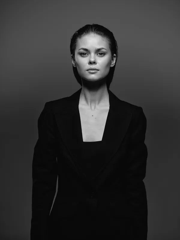 Black and white portrait of a serious woman in a dark jacket with neutral expression and clean background.
