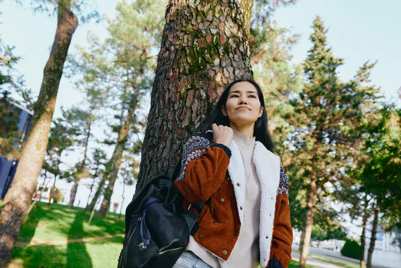 woman outdoors tree park serenity daytime casual nature with backpack jacket sunlit scene for lifestyle travel wellness and nature themes