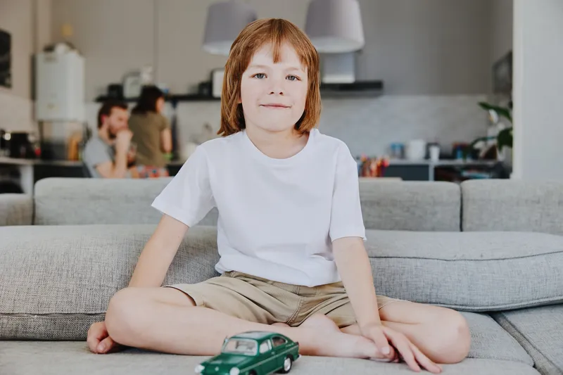 Smiling boy sitting on a sofa, playing with a toy car in a cozy home environment, showcasing happiness and creativity in a modern living space.