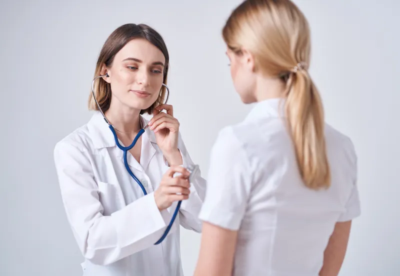 Врач в медицинском халате на светлом фоне и пациентка — блондинка