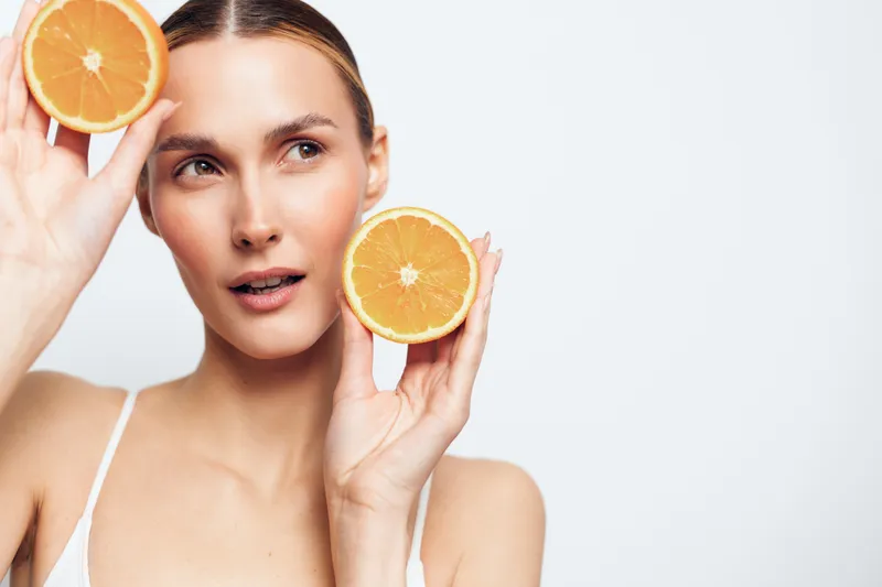 Woman orange citrus skincare beauty facial fresh spa close up, she holds orange slices by her face, clean white background, natural glow, hydration concept