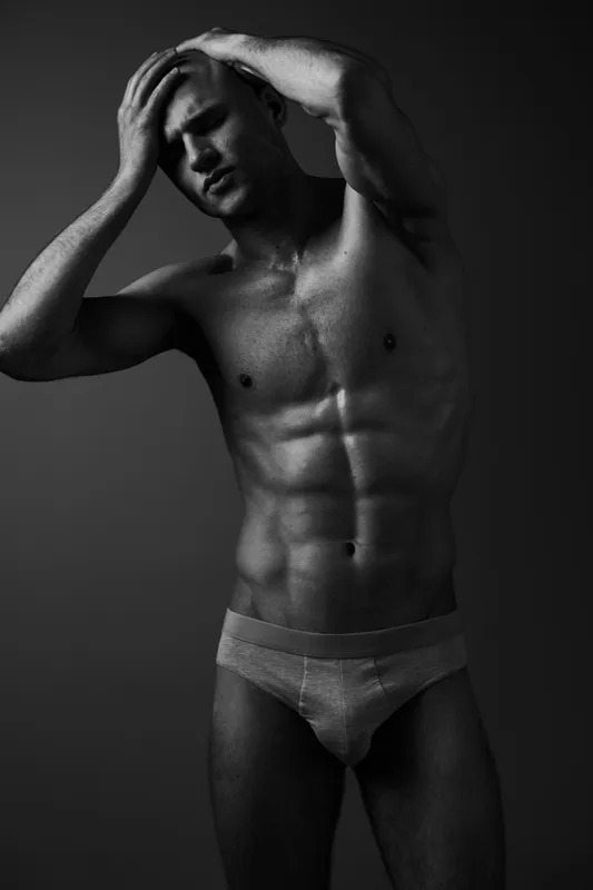 Black and white portrait of a muscular man, posing confidently while expressing strong emotions. The image captures the essence of strength and determination.