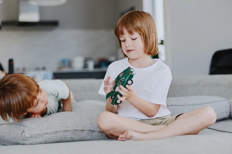 Engaged boy and girl playing with toys on a cozy sofa in a modern living room, showcasing friendship and creativity in a bright and inviting space.