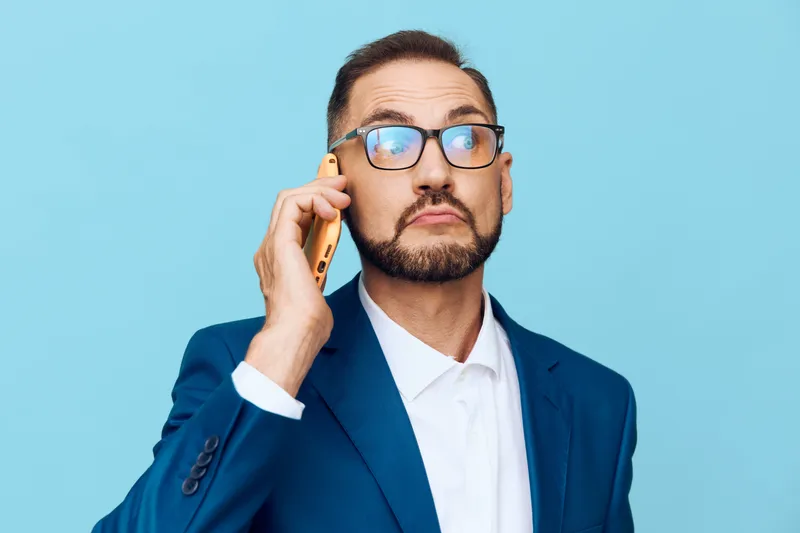 A poised business professional man in a blue suit speaks on a mobile phone against a bright, isolated colored background, conveying focus, confidence, and strategic intent.