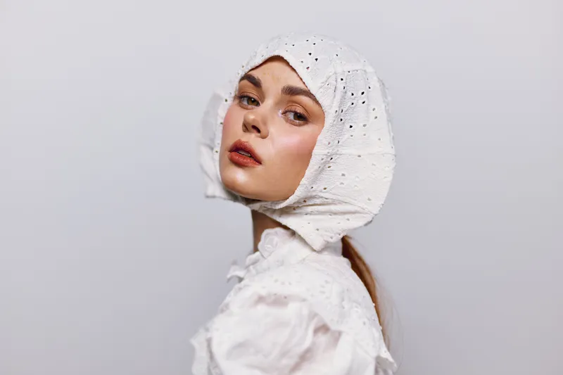 Portrait of a woman wearing a white vintage bonnet and lace blouse, evoking emotions of nostalgia and elegance against a minimalistic background
