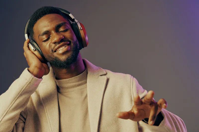 A joyful young African man enjoying music with headphones against a purple background, reflecting relaxation and happiness in a modern lifestyle