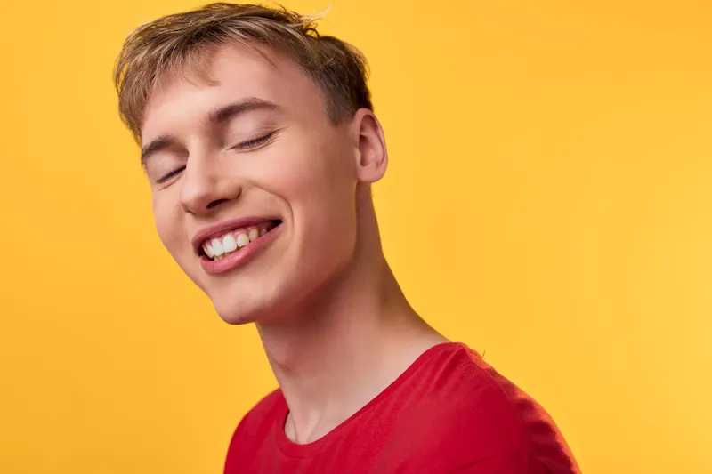 Young man with a bright smile wearing a red shirt against a warm yellow background, conveying joy, confidence and positive energy for lifestyle, advertising and social media campaigns