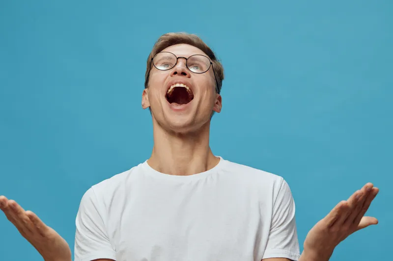 excited man wearing glasses open mouth looking up with raised hands isolated on blue background joyful emotion digital detox concept