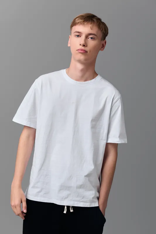 Man wearing a white t shirt stands in a neutral studio with casual confidence, relaxed posture, soft lighting and a minimalist vibe, showcasing simple everyday fashion for lifestyle, clothing