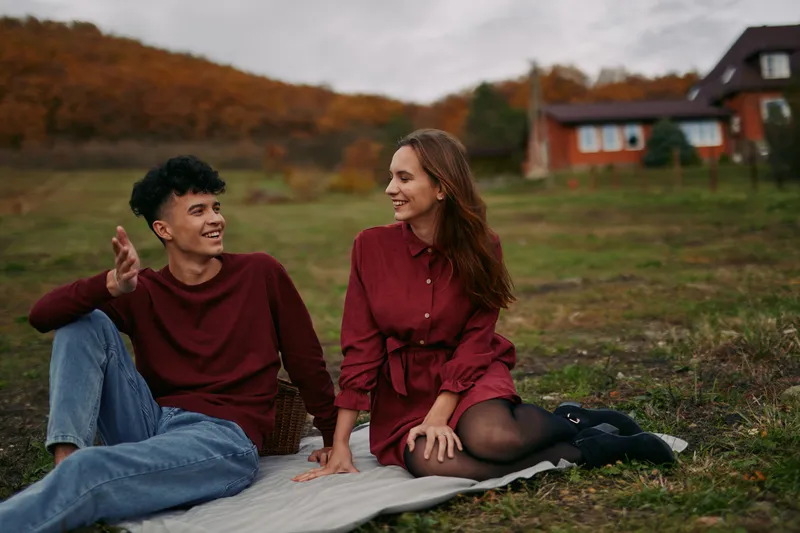 Young couple sharing a genuine moment on a picnic blanket, relaxed conversation and natural smiles conveying real connection and honest emotion in a peaceful autumn countryside setting.
