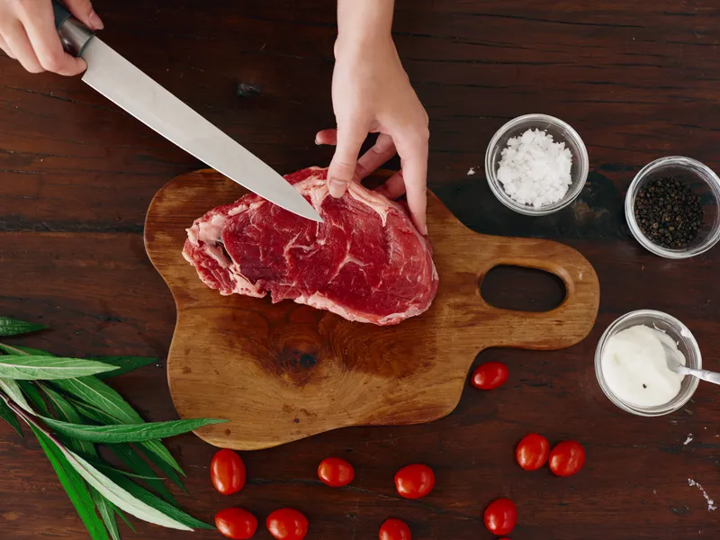 Женщина с ножом в руке нарезает свежее мясо стейка для жарки на кухне