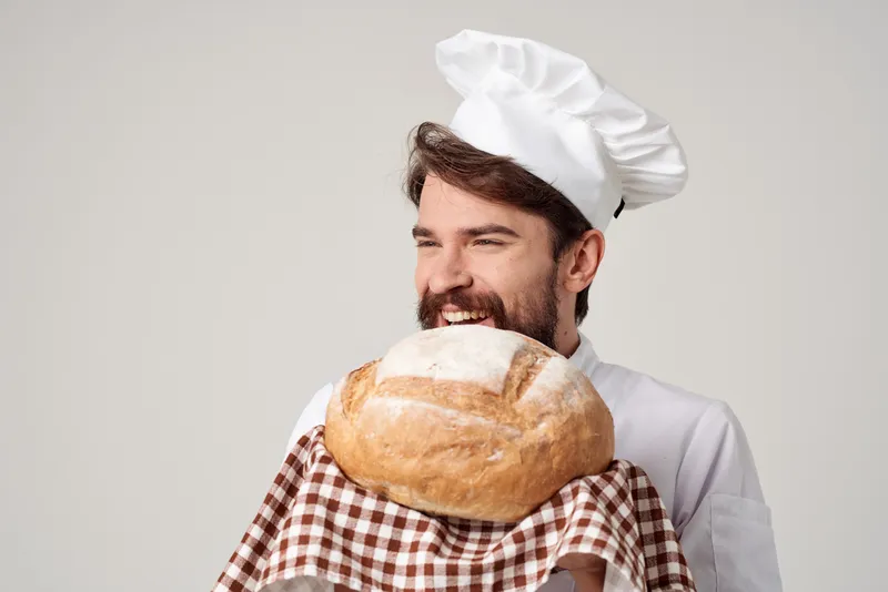 Бородатый мужчина-шеф-повар держит в руке хлеб на изолированном фоне