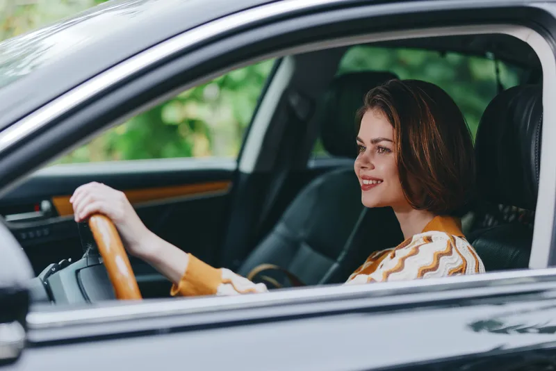 Smiling woman driving a car, hands on the wheel, captured from the interior for a bright, confident road mood and everyday travel.