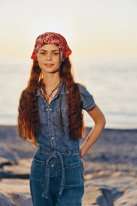 Lifestyle woman in modern boho-western denim street style with a red bandana and long hair at sunset beach, film color tones creating warm, natural mood and authentic vibe.