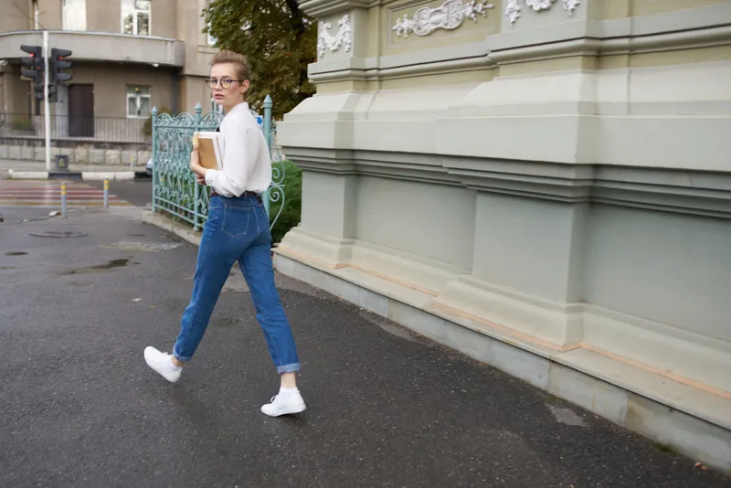 Симпатичная женщина с короткими волосами идёт по улице с книгой в руках