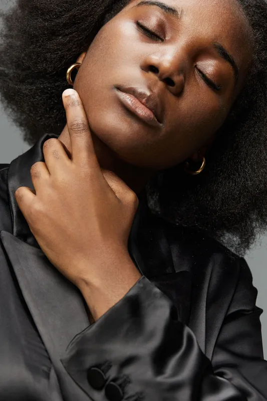 Elegant black woman in a satin black outfit, showcasing confidence and serenity with a neutral background, perfect for fashion and beauty concepts