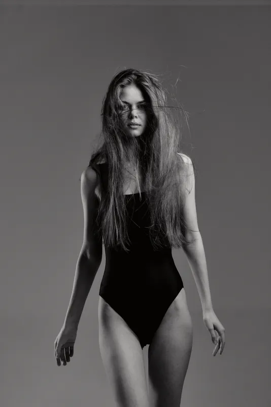 Black and white portrait of a young woman with wet hair in a swimsuit, standing with a serious expression against a plain background.