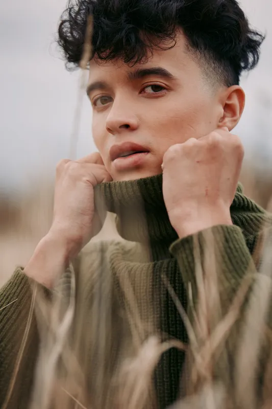 An authentic portrait of a youth in a cozy knit sweater, conveying honest emotion and credibility through natural light and an unposed, calm expression in a rural setting.