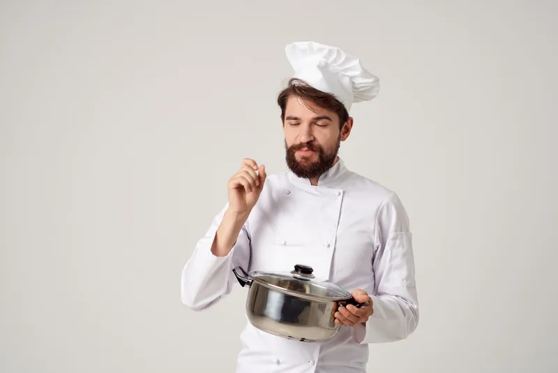 Весёлый повар с кастрюлей в руках на кухне, готовит и работает