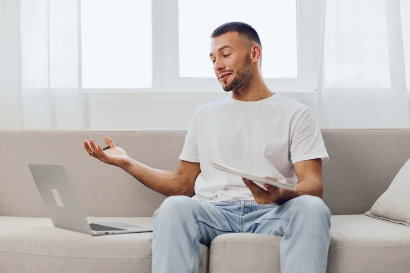 Engaging man discussing ideas while sitting on a couch, wearing casual clothing. The bright background adds a modern touch, reflecting current home office trends.