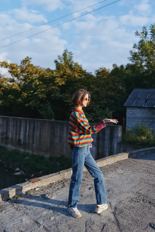 woman striped sweater jeans sunglasses rooftop walking casual outfit young adult smiling outdoors in suburban nature setting, colorful knit, relaxed lifestyle travel and fashion portrait