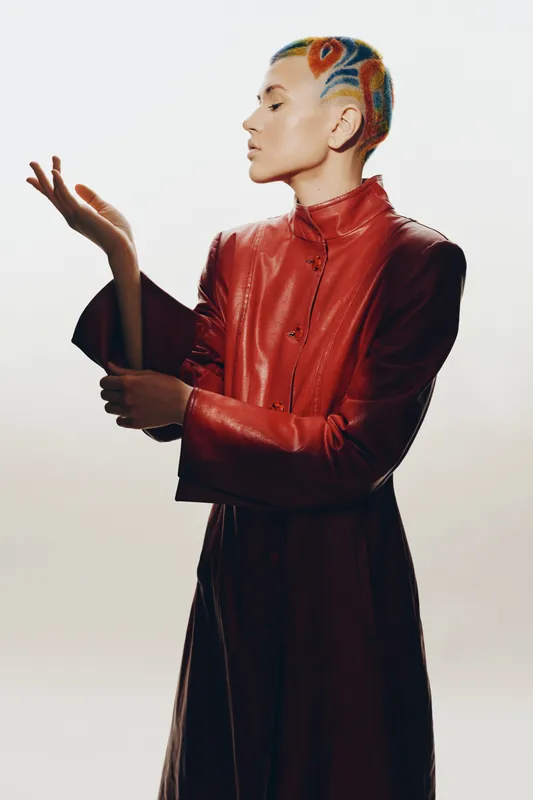 Woman with colorful short hair and red leather coat posing elegantly against a bright background, featuring artistic hairstyle and modern fashion style.