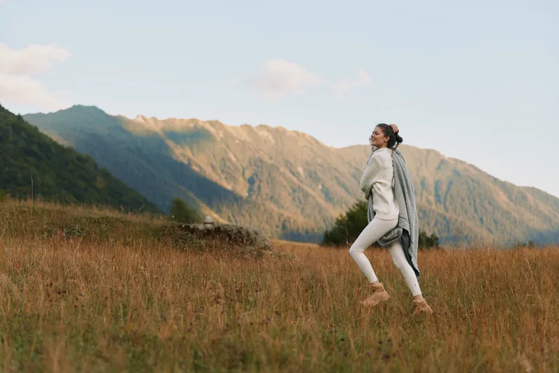 A woman in light clothing runs across a grassy field beside distant mountains, capturing a candid moment of active lifestyle and outdoor freedom.