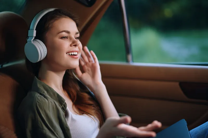 Young woman enjoying music with headphones in a vintage car, smiling and relaxed in a natural setting, vibrant colors, concept of leisure and happiness.