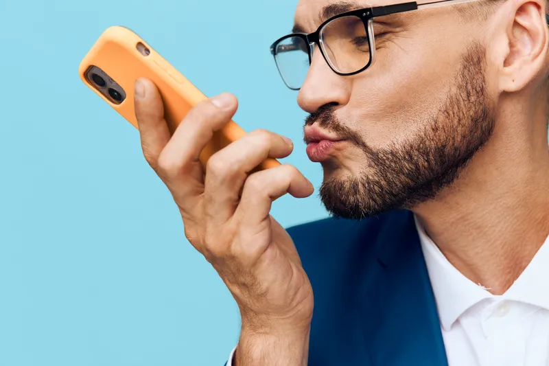 A focused business professional stands against a vivid isolated colored backdrop, conveying confident mood and calm determination while engaging with a mobile device.