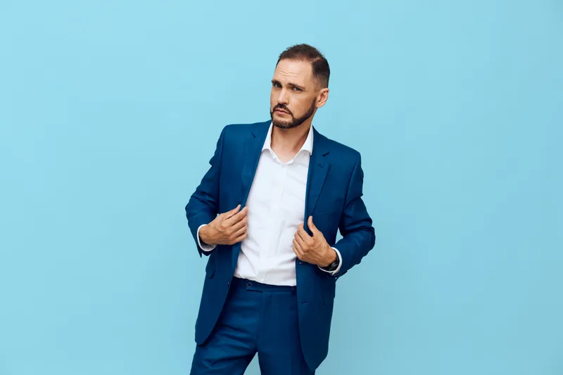 A business professional man stands against a solid colored background, isolated in studio, conveying confidence, focus, calm determination, and ambition.