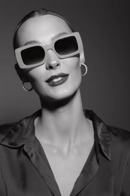 Elegant white woman with pale skin wearing large sunglasses and hoop earrings poses in studio, fashion and style concept.