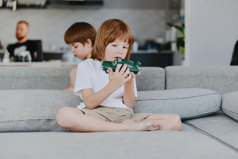 Focused boy playing with car toy, surrounded by family. Relaxed atmosphere in a modern living room with soft colors and comfortable furniture.