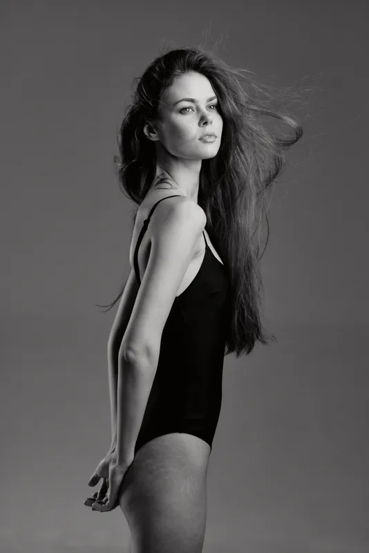 Black and white portrait of a young woman in a black bodysuit with flowing hair and confident expression