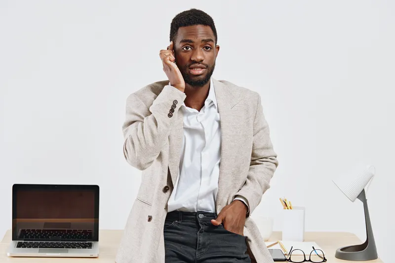 Male professional in casual blazer and shirt holding his head in office setting on a white background, looking concerned or confused. Business, communication, workplace, stress, office life, personali