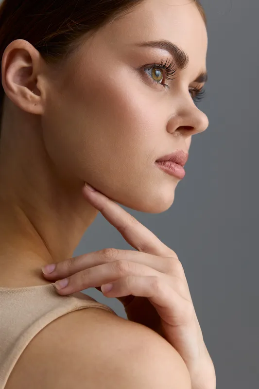 beauty woman in beige top with flawless skin and thoughtful expression, natural makeup, side profile close-up, soft lighting on gray background