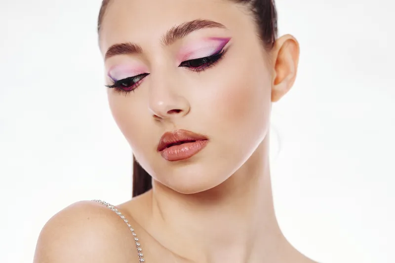 Young woman with creative purple eyeshadow and pearl skin wears delicate diamond strap. Studio portrait on white. Concept for beauty fashion editorial, makeup trends, and charm.