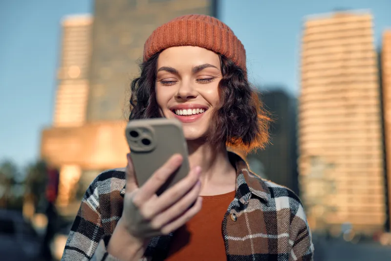 woman smartphone smile urban candid authenticity golden hour glow, beanie plaid shirt, mindful living and emotional storytelling of modern city genuine connection.